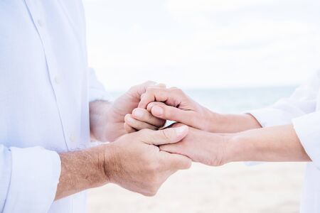 cropped view of senior couple in white shirts holding hands under blue skyの写真素材