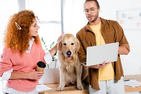 attractive woman stroking cute golden retriever and businessman holding laptop in office