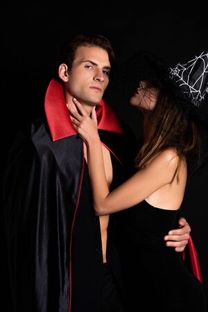 woman in witch hat touching neck of man in halloween costume isolated on blackの写真素材