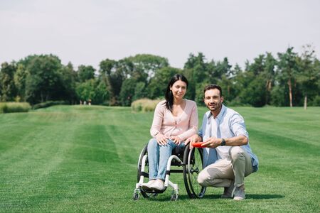 smiling man holding flying disc near young disabled girlfriend in park