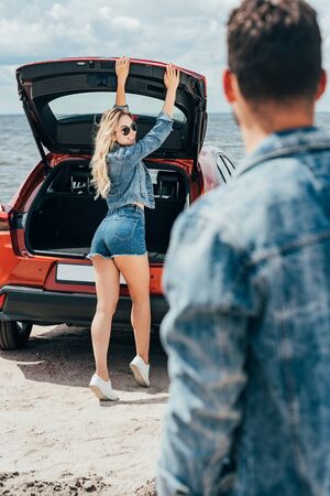 selective focus of attractive woman in denim jacket smiling and looking at man