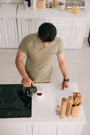 overhead view of young man pouring coffee in cup while standing near cooking surface in kitchenの写真素材