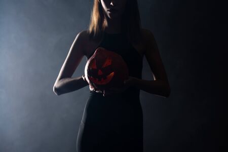 cropped view of woman with horns holding spooky pumpkin on black with smokeの写真素材