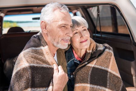 smiling senior couple sitting in car with blanketの写真素材