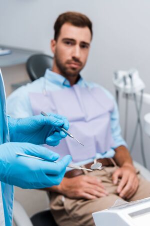 selective focus of dentist in blue latex gloves holding dental instruments near manの写真素材
