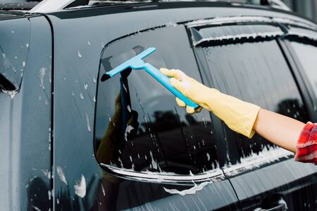 cropped view of woman washing black car with squeegee