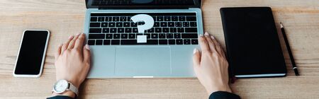 panoramic shot of woman near question mark on laptop near smartphone and notebook の写真素材