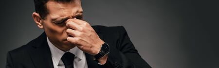 tired african american businessman in suit rubbing his eyes on dark background, panoramic shotの写真素材