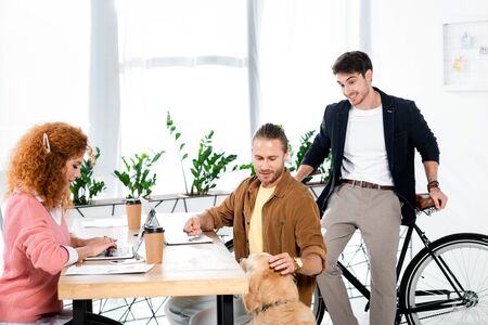 attractive woman using laptop and friends stroking golden retriever in office