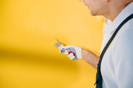 cropped view of young painter painting wall in yellow color with paintbrushの写真素材