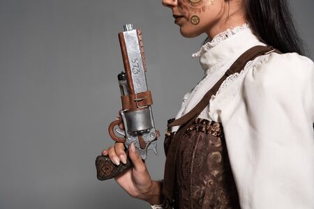 cropped view of steampunk woman holding vintage pistol isolated on greyの写真素材