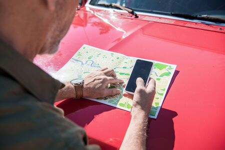 cropped view of man standing near red car with map and using smartphone with blank screen