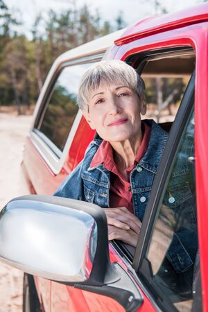 senior woman in denim jacket looking from car window
