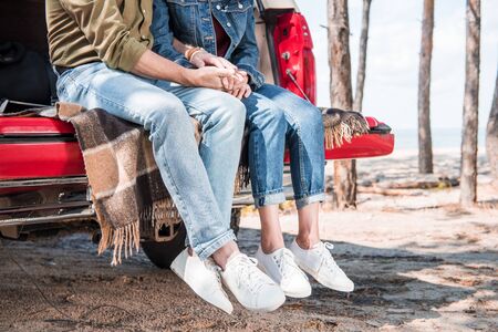 cropped view of senior couple sitting on blanket in car and holding hands in sunny dayの写真素材