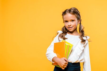 smiling and cute kid holding books isolated on orangeの写真素材
