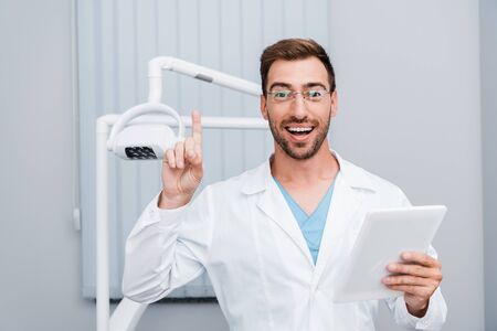 cheerful bearded man in white coat and glasses gesturing while holding digital tabletの写真素材