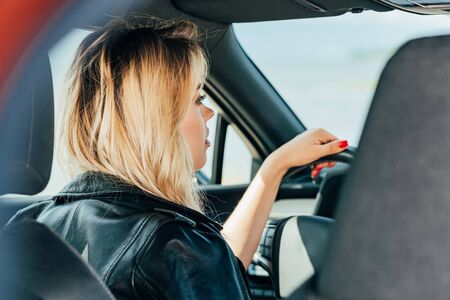 back view of blonde woman in black jacket driving carの写真素材