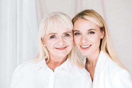 cheerful blonde grandmother and granddaughter together in total white outfitsの写真素材
