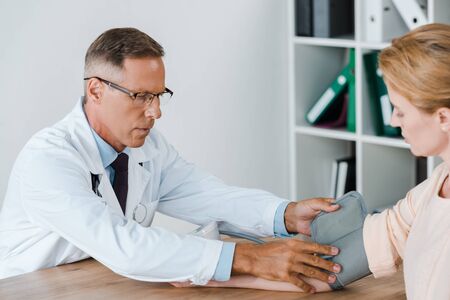 selective focus of doctor measuring blood pressure of woman on table in hospitalの写真素材