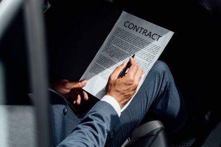 partial view of african american businessman in suit reading contract in carの写真素材