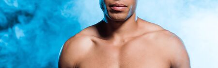 panoramic shot of sexy mixed race man standing on blue with smokeの写真素材