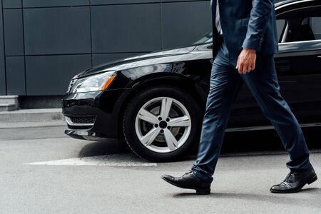 cropped view of african american businessman in suit walking along parking near black carの写真素材
