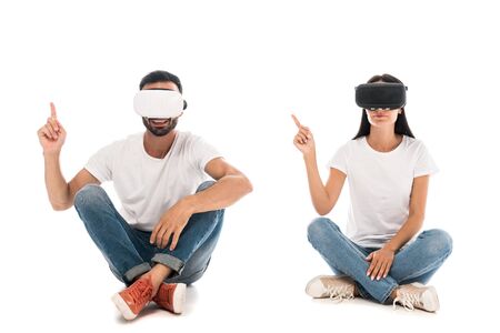 happy man sitting with woman while using virtual reality headsets and pointing with fingers on whiteの写真素材