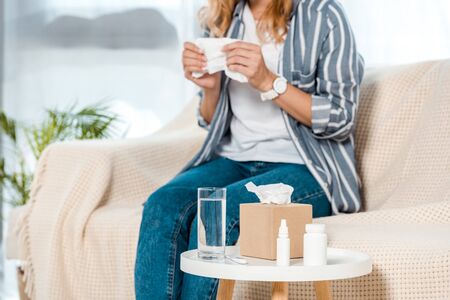 cropped view of woman sitting on sofa and holding napkin near glass with waterの写真素材