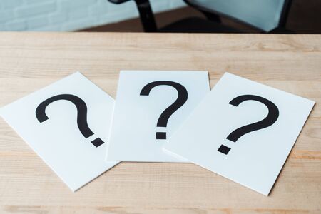 black question marks on white papers on wooden table 