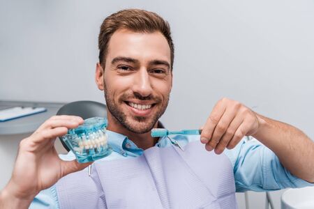 happy man holding tooth model and toothbrush in clinic
