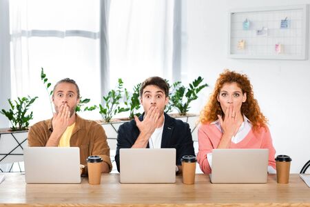 three shocked friends sitting at table and obscuring faces