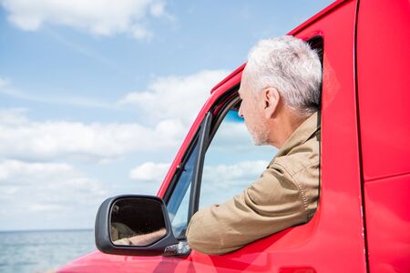 senior man looking at river from red carの写真素材