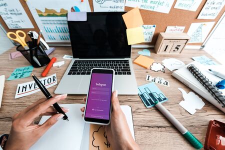 KYIV, UKRAINE - JULY 23, 2019: cropped view of woman holding smartphone with instagram app near sticky notes with lettering and laptop with blank screenのeditorial素材