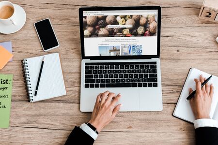 KYIV, UKRAINE - JULY 23, 2019: top view of woman using laptop with depositphotos website near smartphone with blank screenのeditorial素材