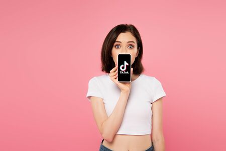 KYIV, UKRAINE - JULY 3, 2019: shocked girl holding smartphone with tiktok logo isolated on pinkのeditorial素材