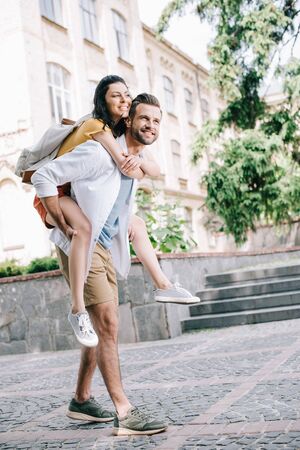 happy bearded man piggybacking cheerful girl near buildingの写真素材