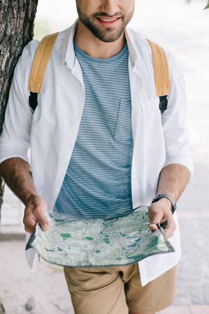 cropped view of happy bearded traveler holding map near treeの写真素材