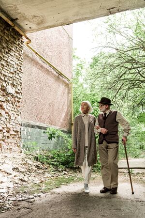 retired woman and senior man with walking stick walking near green treesの写真素材