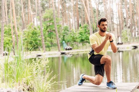 athletic sportsman in sportswear exercising near lake in forestの写真素材