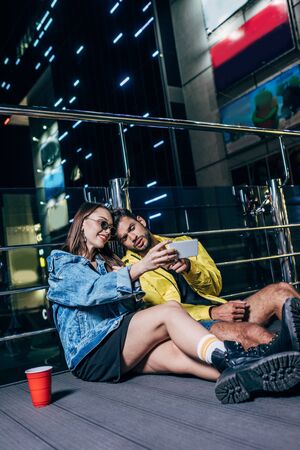 handsome boyfriend and attractive girlfriend smiling and taking selfie in night cityの写真素材