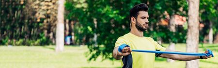 panoramic shot of bearded man holding suspension straps while exercising in parkの写真素材