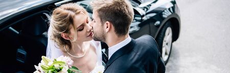 panoramic shot of attractive bride and handsome bridegroom kissing outsideの写真素材