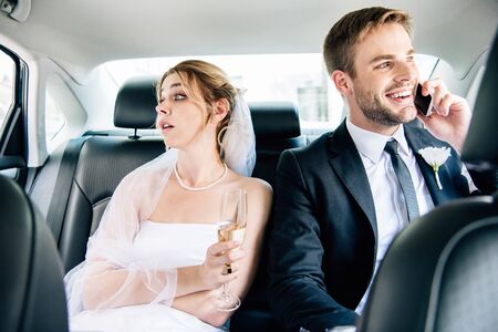 attractive bride looking away and handsome bridegroom talking on smartphone