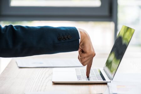 cropped view of man pointing with finger at laptop on table