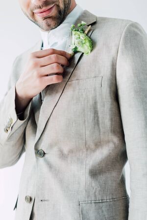cropped view of bridegroom in suit holding floral boutonniere isolated on greyの写真素材