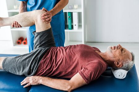 cropped view of doctor holding leg of mature man with closed eyesの写真素材