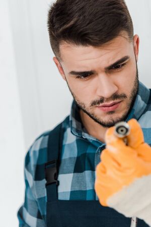 selective focus of repairman in rubber glove looking at metal hose