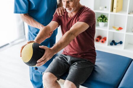 selective focus of bearded middle aged man exercising with ball near doctorの写真素材