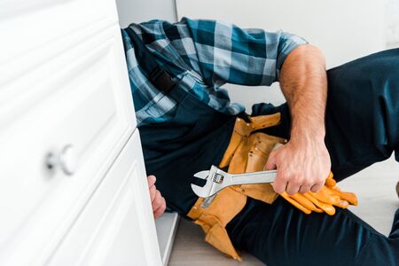 cropped view of handyman holding adjustable wrench near kitchen cabinet