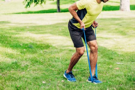 cropped view of bearded man exercising with suspension straps in park